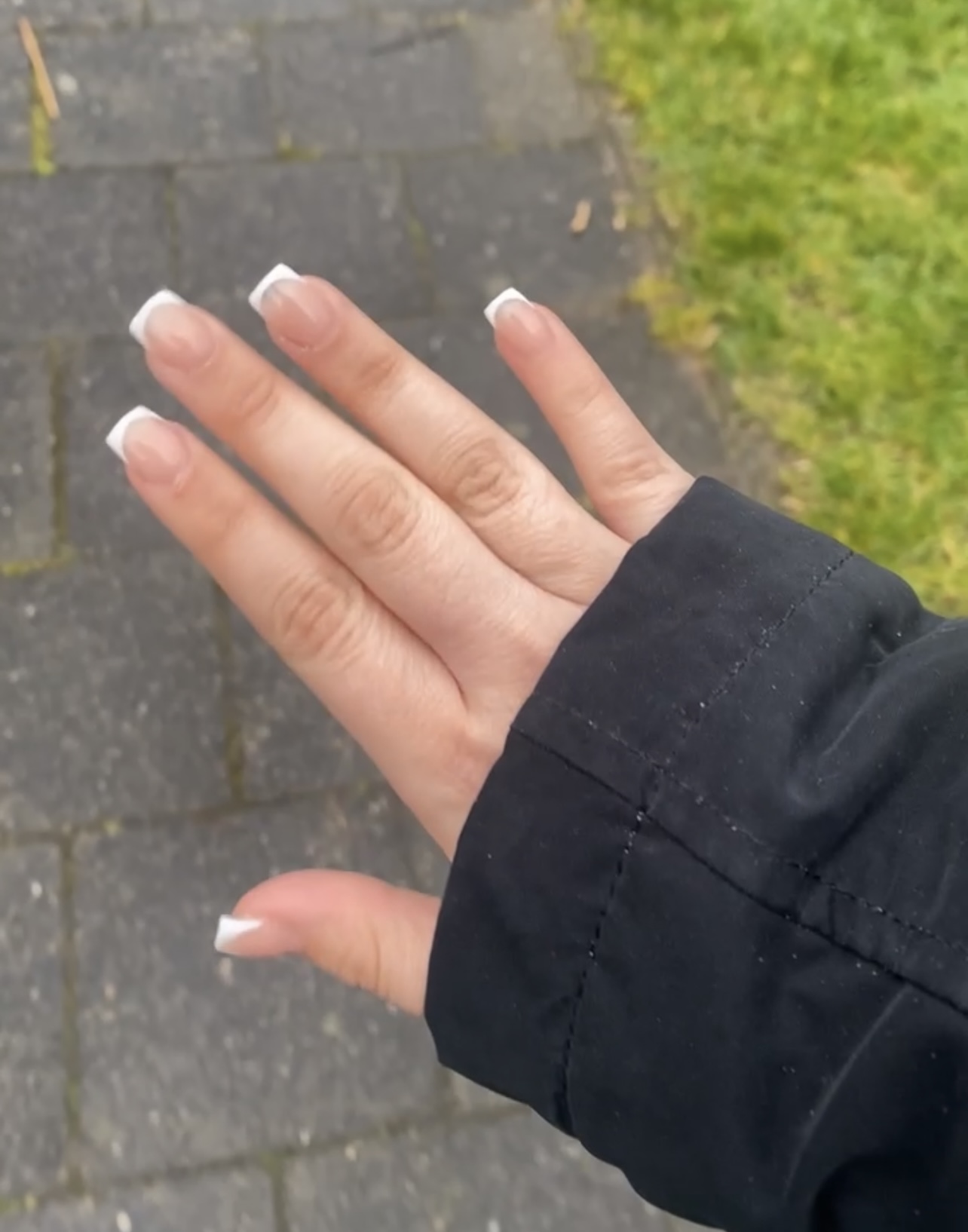 Hand met een witte french manicure, buiten op de stoep